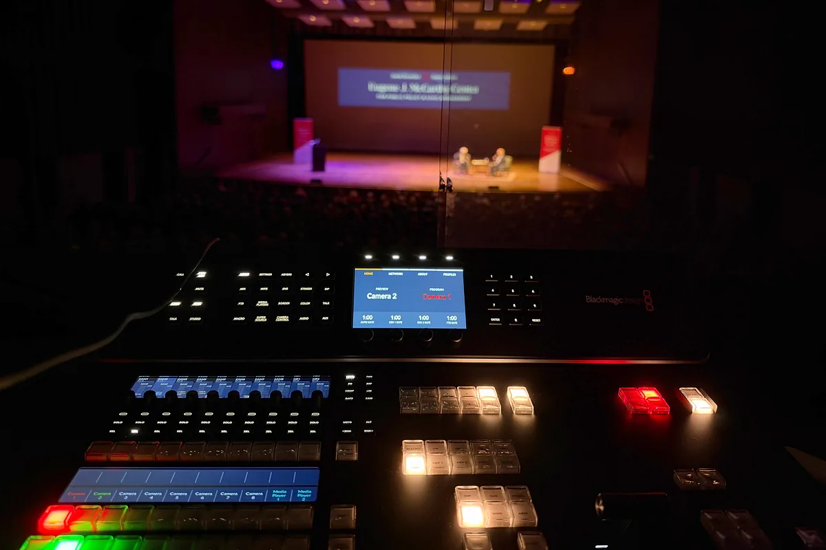 Production switcher lit in the control room with the McCarthy Lecture stage beyond the glass